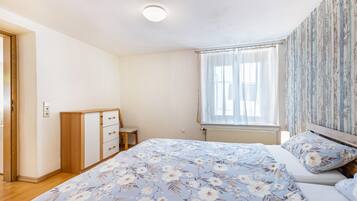 A bedroom with a bed, a dresser, a window with curtains, and a radiator.