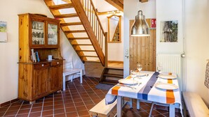A dining area with a wooden table set for four, a bench, and a staircase leading to an upper level. - Holiday Home 'Forsthof Schulte' with Private Terrace, Private Garden and Wi-Fi (Pronstorf)