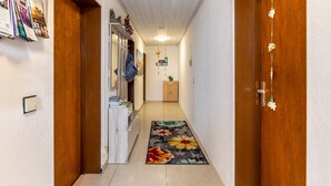 Un couloir avec des portes en bois, un sol carrelé, un tapis à motifs floraux, un meuble en bois et une plante suspendue.