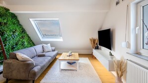 Ein modernes Wohnzimmer mit grauem Sofa, einem Holztisch, einem weißen Teppich, einem Fernseher und einer grünen Wand.