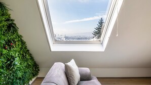 Ein Zimmer mit Oberlicht, einem grauen Sofa und einer grünen Wand mit Pflanzen.