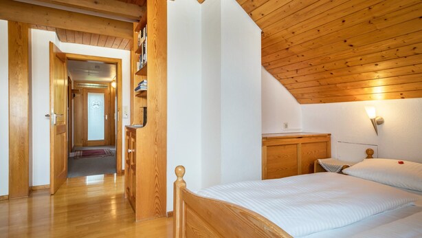 Quarto com teto de madeira, uma cama, mesa de cabeceira e luminária na parede.