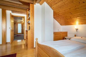 Un dormitorio con techo de madera, una cama, una mesita de noche y una lámpara fijada a la pared.