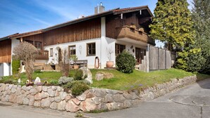 A traditional wooden house with a stone wall, a balcony, and a well-maintained garden. - Studio Apartment 'Lackner' with Mountain View, Balcony and Wi-Fi (Teisendorf)