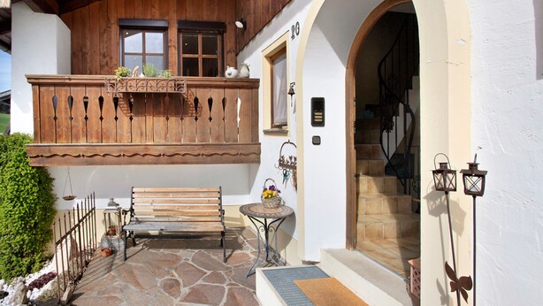 A wooden balcony with a bench, a small table with a flower arrangement, and a staircase leading to an interior. - Studio Apartment 'Lackner' with Mountain View, Balcony and Wi-Fi (Teisendorf)