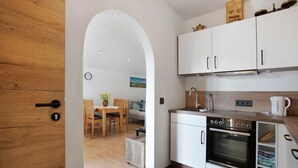 A modern kitchen with white cabinets, a built-in oven, and a dining area with a wooden table and chairs. - Studio Apartment 'Lackner' with Mountain View, Balcony and Wi-Fi (Teisendorf)