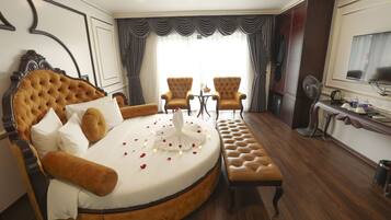 A luxurious bedroom with a large round bed, two armchairs, a small table, and a television.