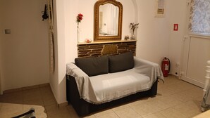 Une pièce comprenant un canapé, une cheminée, un miroir, un extincteur et une porte avec un rideau.