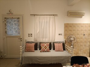A bedroom with a bed, a window with a curtain, an air conditioner, and a wall-mounted fan.
