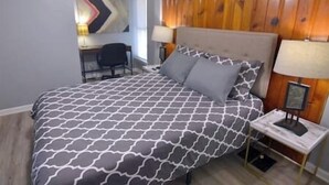 A bedroom with a patterned bedspread, a wooden headboard, two bedside lamps, and a desk with a chair.