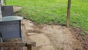 A patio area with a metal table and chairs, a concrete path leading to a grassy area, and a wooden fence.