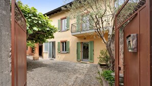 A courtyard with a building featuring a balcony, a wooden chair, and a gravel ground. - Holiday Home 'Casa Romantica' with Private Terrace, Balcony and Wi-Fi (Ispra VA)