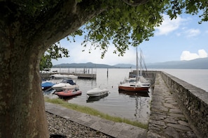 A calm marina with boats docked, a stone wall, and a tree in the foreground.