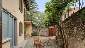 A courtyard with wicker furniture, a stone wall, and a building with a door and windows. - Holiday Home 'Casa Romantica' with Private Terrace, Balcony and Wi-Fi (Ispra VA)