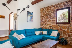 A living room with a blue sofa, a wooden coffee table, a stone wall, and a window with a view of trees. - Villa 'Chez Tao' with Pool, Garden, Terrace & Wi-Fi (Bandol)