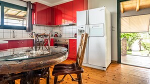 Une cuisine avec des meubles de rangement rouges, un réfrigérateur blanc, une table à plateau en verre et une chaise en bois.