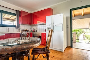 Eine Küche mit roten Schränken, einem weißen Kühlschrank, einem Glastisch und einem Holzbstuhl.