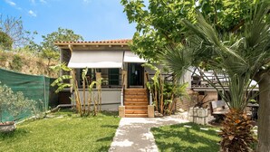Une maison avec un chemin pavé menant à l’entrée, entourée de verdure et dotée d’un petit patio.