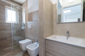Ein modernes Badezimmer mit Dusche, Toilette, Bidet und einem großen Spiegel.