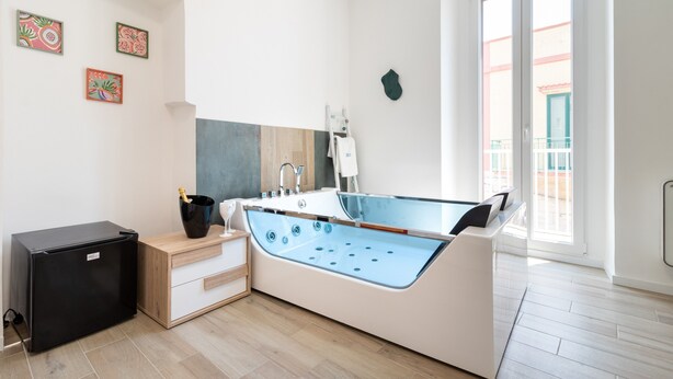 Un baño moderno con bañera, un refrigerador negro pequeño, un armario de madera y un ventanal grande.