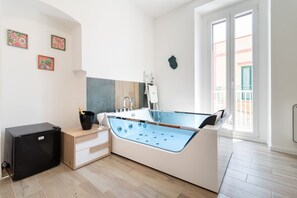Un baño moderno con bañera, un refrigerador negro pequeño, un armario de madera y un ventanal grande.