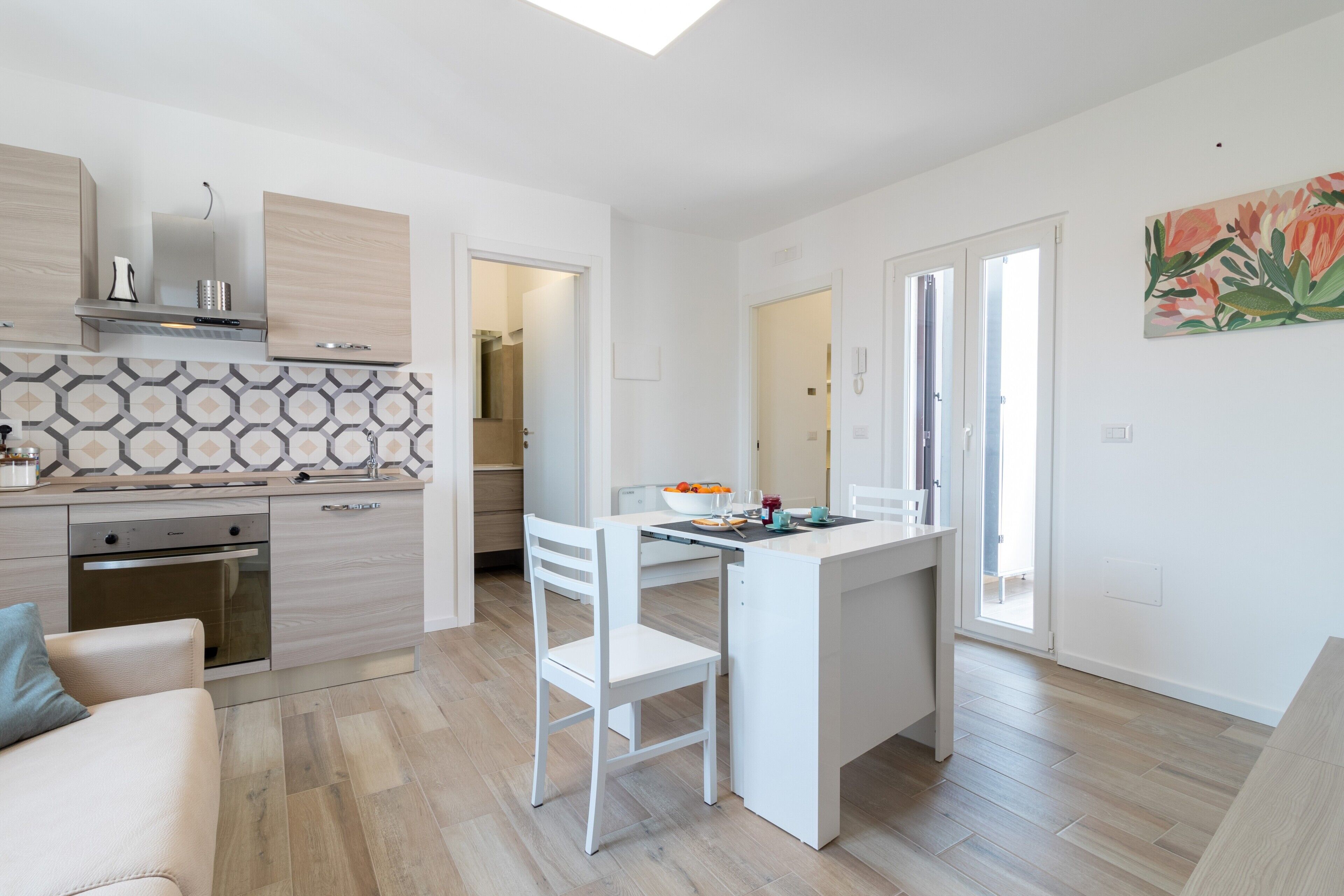A modern kitchen with a dining area, wooden flooring, and a view to the outside.