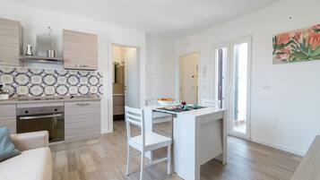 A modern kitchen with a dining area, wooden flooring, and a view to the outside.