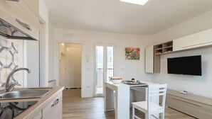 Una cocina moderna con lavavajillas incorporado, una zona de comedor con mesa y sillas blancas y un televisor de pantalla plana montado en la pared.