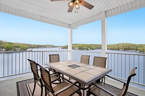 A covered outdoor area with a table and chairs, overlooking a body of water and a distant shoreline.