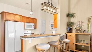 Una cucina con mobili in legno, un frigorifero bianco, un forno a microonde e un'area bar con sedie in vimini.