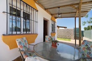 A covered patio with a glass table and chairs, a potted plant, and a view of the backyard. - Holiday Home 'Casa Manoli 3 Chiclana' with Private Terrace and Private Garden (Chiclana de la Frontera)