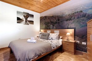 Ein Schlafzimmer mit Bett, Nachttisch, Kommode und einer großen Wandmalerei einer Berglandschaft.