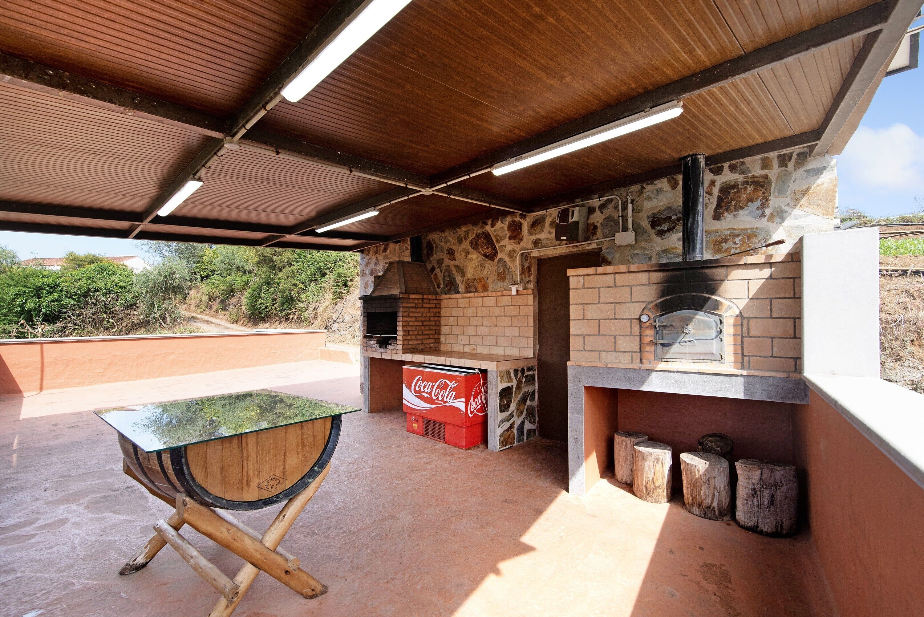 Terrassa exterior amb forn de maó, nevera de Coca-Cola i taula de fusta.