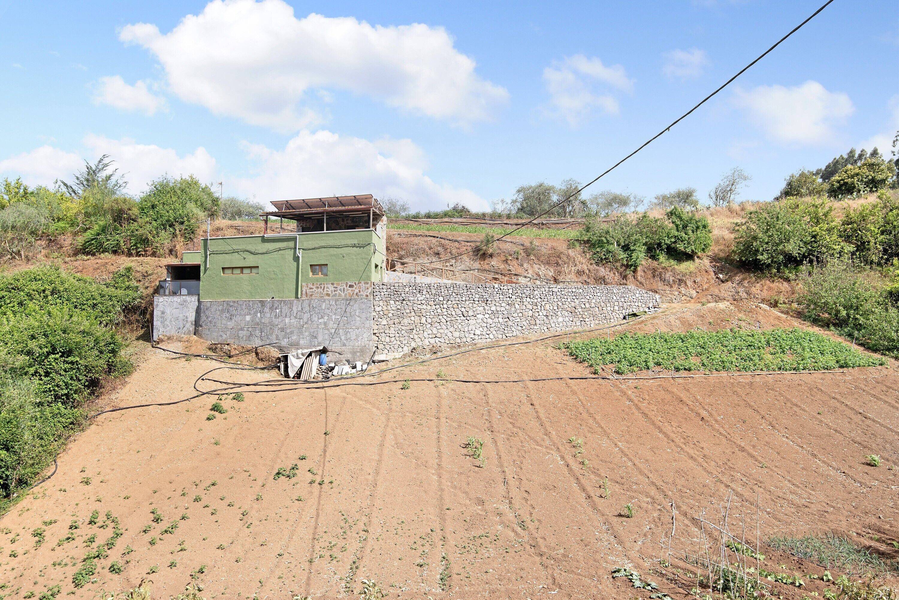 Entorno rural con un edificio verde, muros de piedra y un campo.