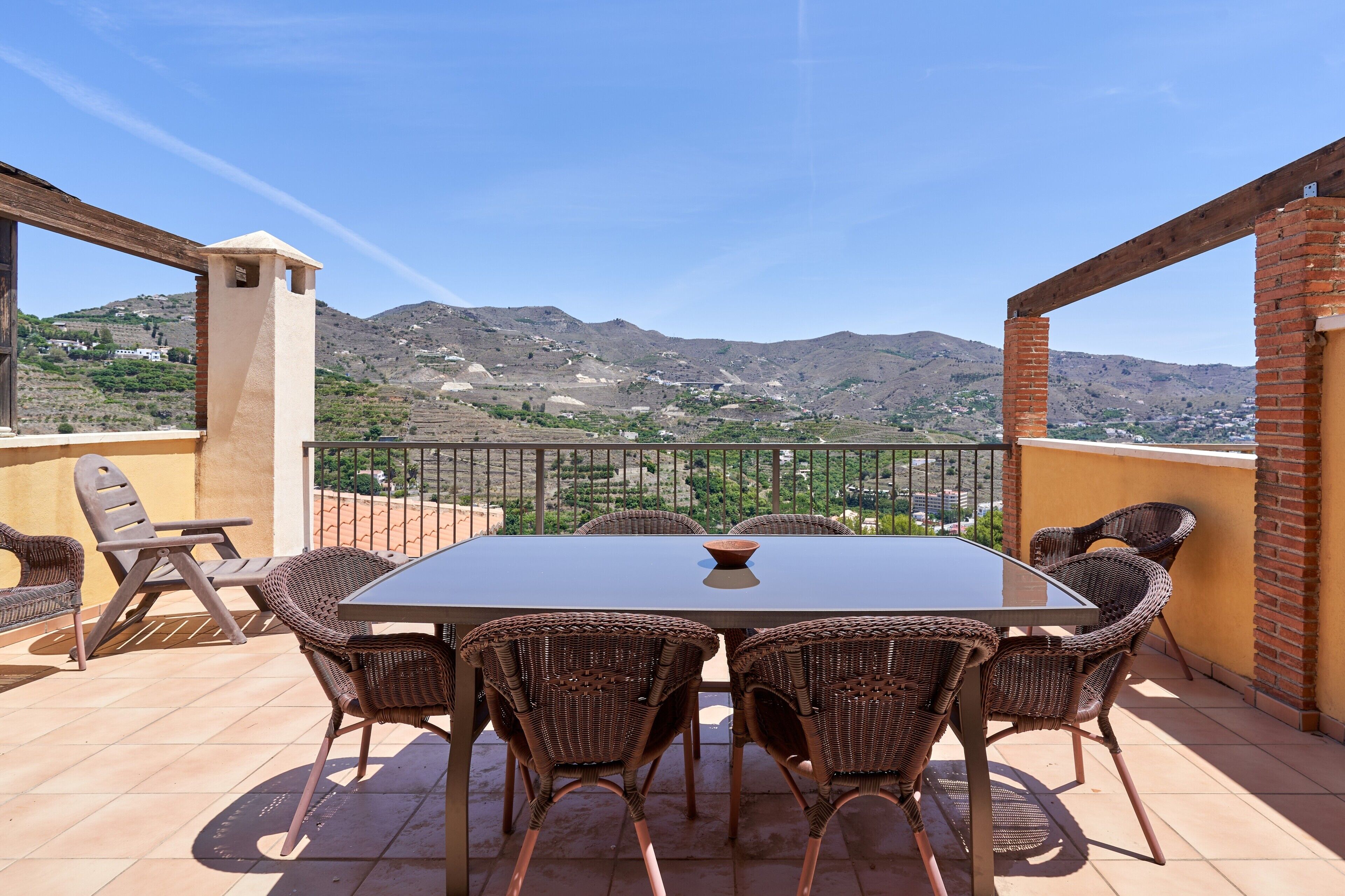 A terrace with a table and chairs, a view of hills, and a brick wall.