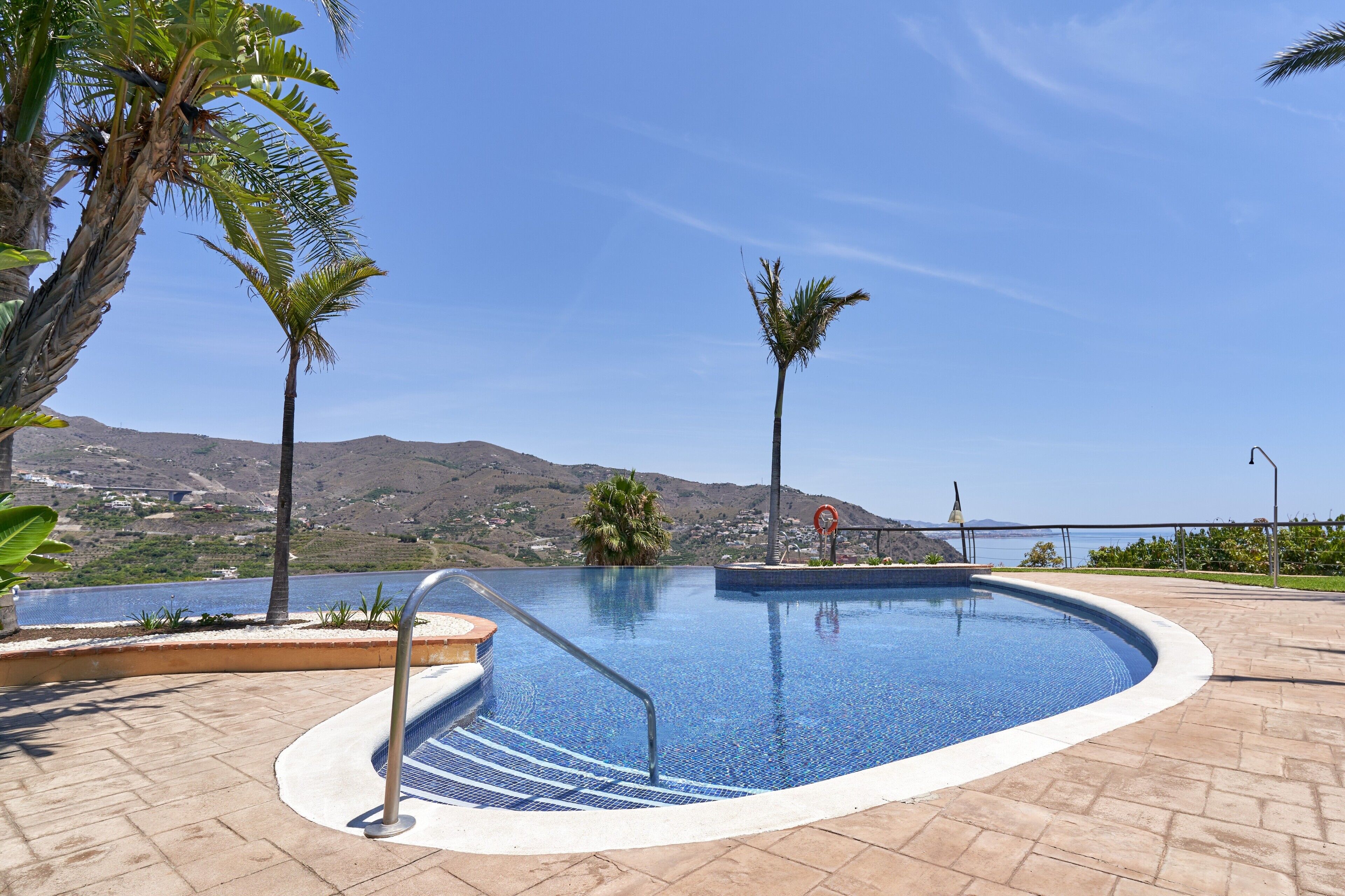 Una piscina con una vista despejada del paisaje circundante, que incluye palmeras y colinas al fondo.