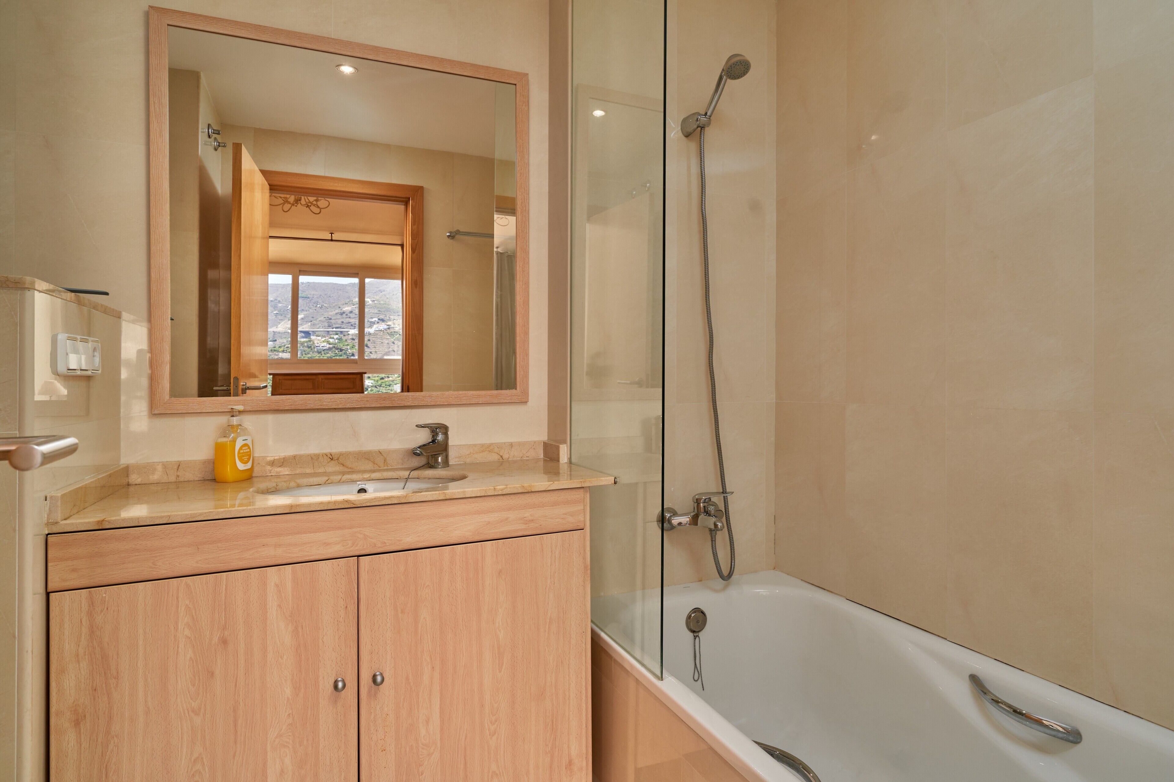 A bathroom with a bathtub, a glass-enclosed shower, a wooden vanity, and a large mirror.