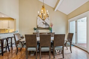 A dining area with a chandelier, a painting, and a view of the outside. - Condo with Fireplace & Golf Views, Fox Hollow (Quechee)