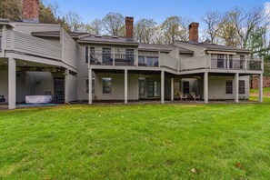 A two-story house with a covered porch, a small deck, and a fenced backyard. - Condo with Fireplace & Golf Views, Fox Hollow (Quechee)