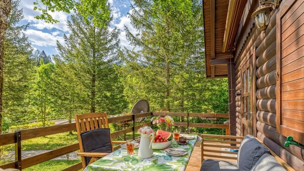 A wooden deck with a table set for dining, surrounded by chairs, and a view of a forest.