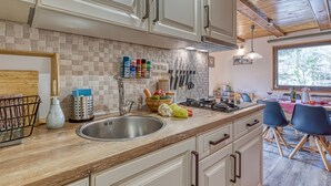 A modern kitchen with a wooden countertop, stainless steel sink, and white cabinets. There are various kitchen utensils and a window providing natural light.