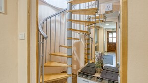 A spiral staircase with wooden steps and metal railings, leading to a landing area with a shoe rack and a mirror.