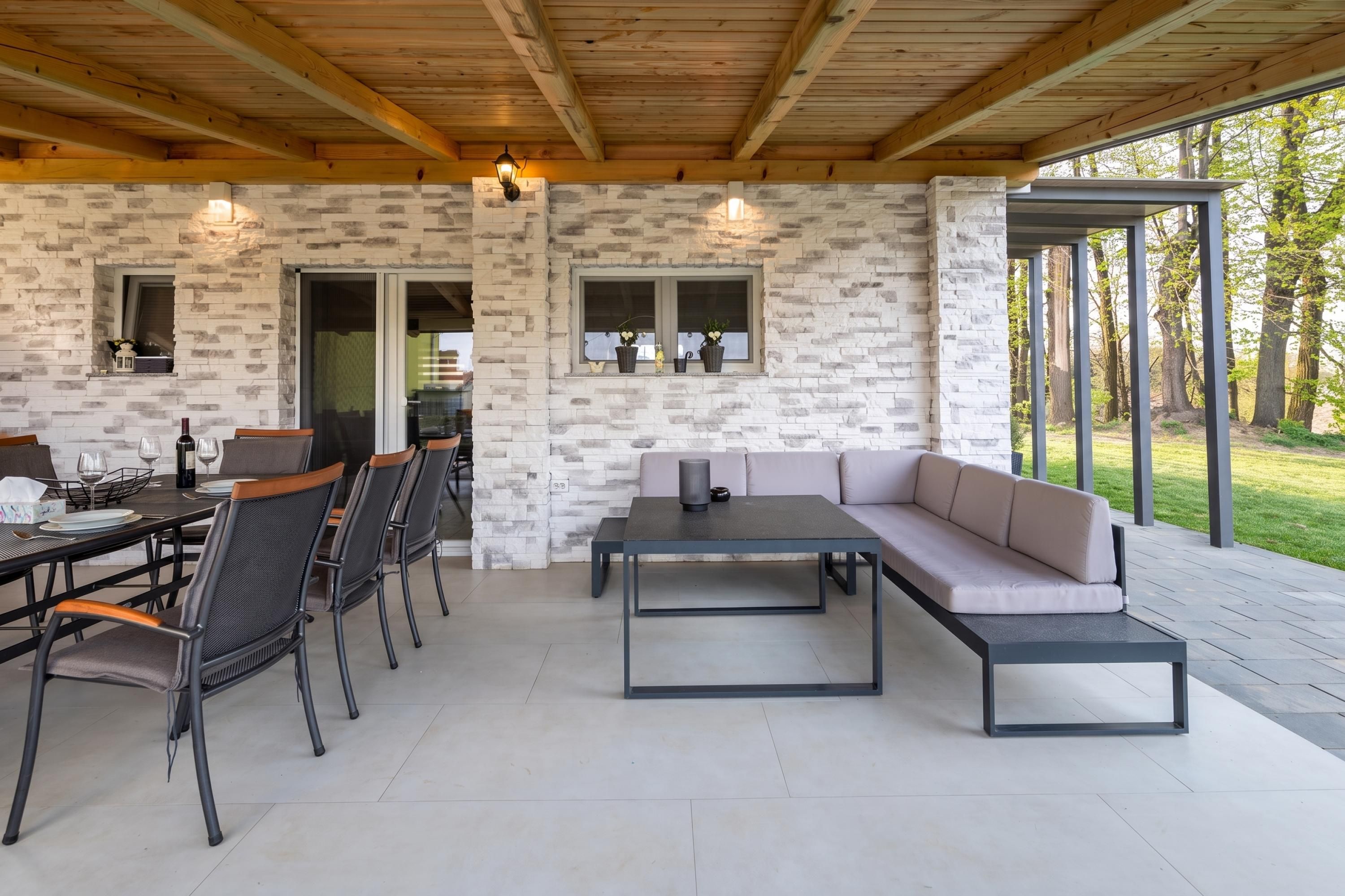 Une terrasse extérieure avec des murs en pierre, une table à manger avec des chaises, un canapé et une lampe de table.