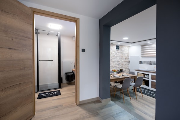 A modern kitchen with a stone accent wall, wooden flooring, and a dining area with chairs and a table.