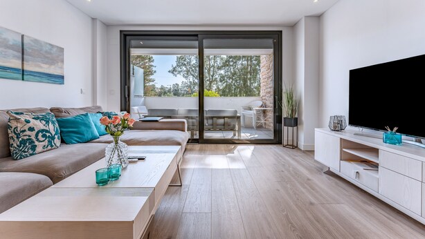 A modern living room with a sofa, coffee table, TV, and a sliding glass door leading to an outdoor area. - 206 Navi Golf – Family-Friendly Retreat with Pool & Kids Park (La Cala de Mijas)