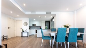 A modern kitchen with white cabinets, a microwave, and a dining area with teal chairs and a white table. - 206 Navi Golf – Family-Friendly Retreat with Pool & Kids Park (La Cala de Mijas)