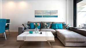 A modern living room with a sofa, coffee table, and a painting of a beach scene. - 206 Navi Golf – Family-Friendly Retreat with Pool & Kids Park (La Cala de Mijas)