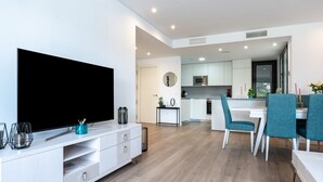 A modern living room with a flat-screen TV, white cabinetry, teal chairs, and a kitchen area with white cabinets and a microwave. - 206 Navi Golf – Family-Friendly Retreat with Pool & Kids Park (La Cala de Mijas)