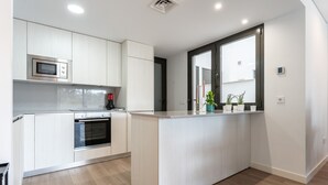A modern kitchen with white cabinetry, a built-in microwave, an oven, and a large window. - 206 Navi Golf – Family-Friendly Retreat with Pool & Kids Park (La Cala de Mijas)