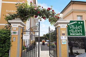 A gated entrance to Villa Alda Apartments with a sign indicating the name and a view of the street.